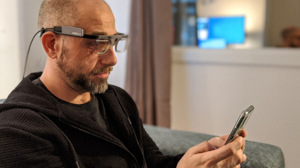 A man in the CTI UX lab, wearing eye tracking glasses and holding a mobile phone